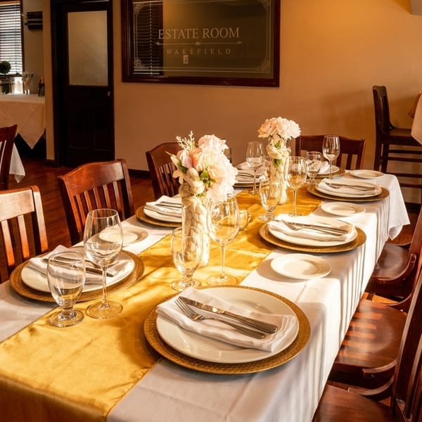 Elegant dining room with set tables, white tablecloths, gold runners, and floral centerpieces.