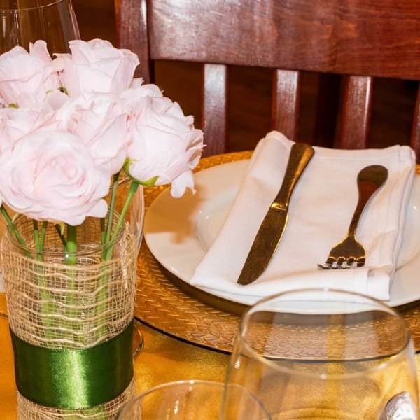 Elegant table setting with pink roses, gold charger, white plate, and gold cutlery.