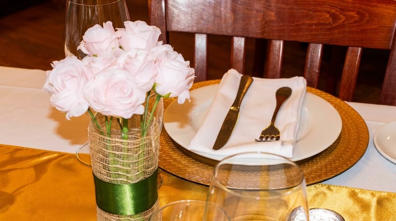 Elegant table setting with pink roses, gold charger, white plate, and gold cutlery.