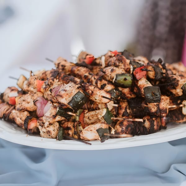 Grilled chicken and vegetable skewers, including zucchini, red onion, and bell peppers, on a white platter.