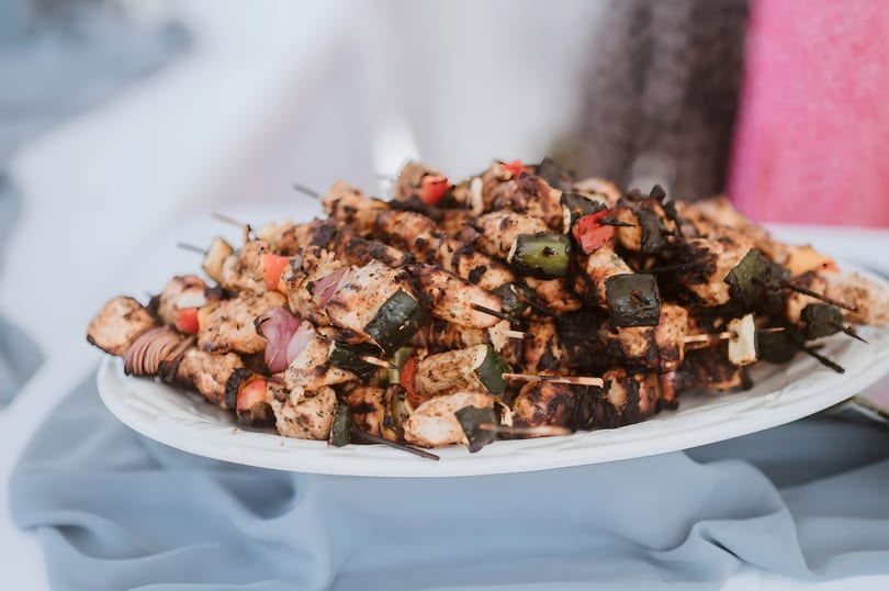 Grilled chicken and vegetable skewers, including zucchini, red onion, and bell peppers, on a white platter.
