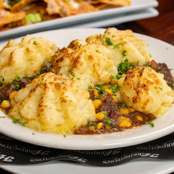 Shepherd's pie with mashed potato peaks, ground meat, corn, and parsley on a white plate.
