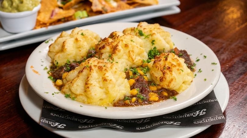 Shepherd's pie with mashed potato peaks, ground meat, corn, and parsley on a white plate.