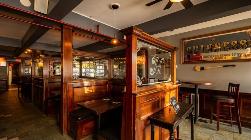 Cozy pub interior with dark wood booths, a Guinness mirror, and warm lighting.