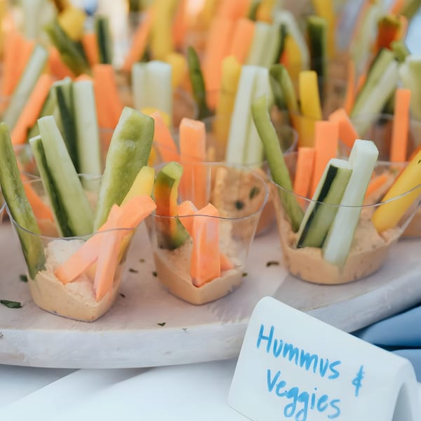 Individual cups of hummus with carrot, cucumber, and yellow bell pepper sticks, labeled "Hummus & Veggies".