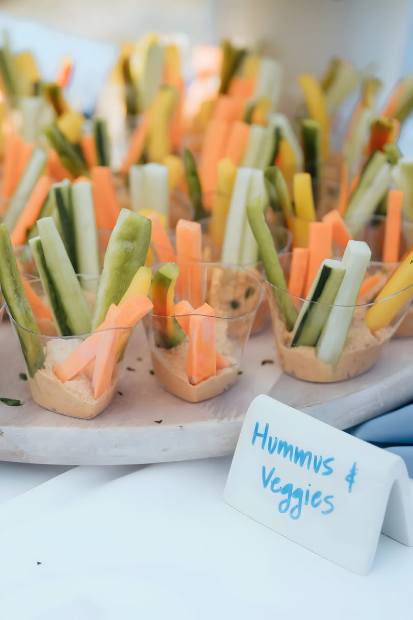 Individual cups of hummus with carrot, cucumber, and yellow bell pepper sticks, labeled "Hummus & Veggies".