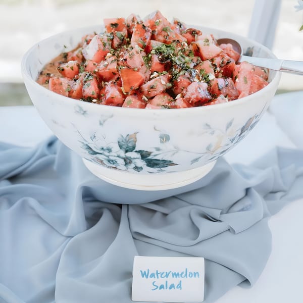 A large bowl of watermelon salad with herbs and feta, on a table with a blue cloth.