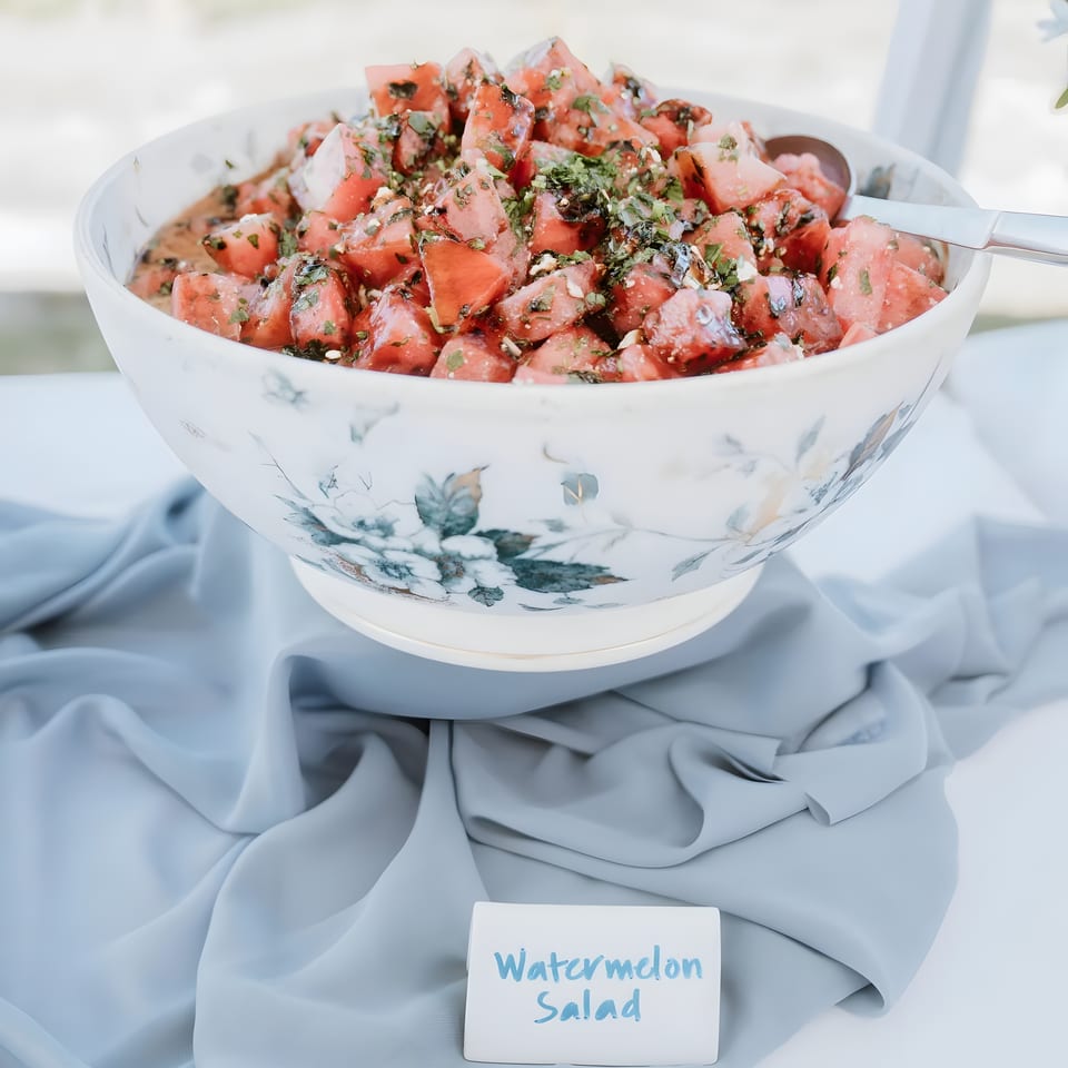 A large bowl of watermelon salad with herbs and feta, on a table with a blue cloth.