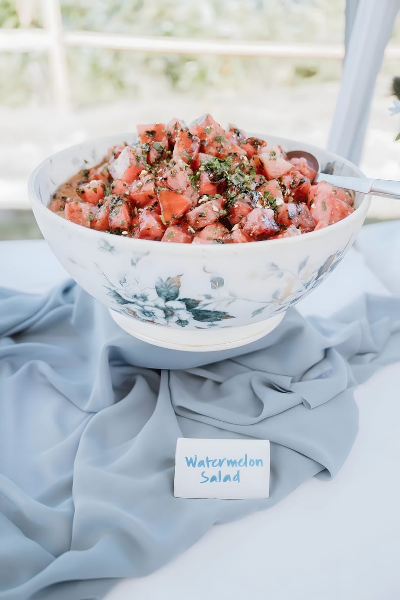 A large bowl of watermelon salad with herbs and feta, on a table with a blue cloth.
