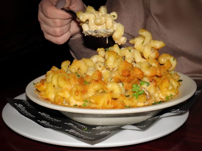 A person spoons creamy mac and cheese with a crispy topping from a large white bowl at Harrington's.