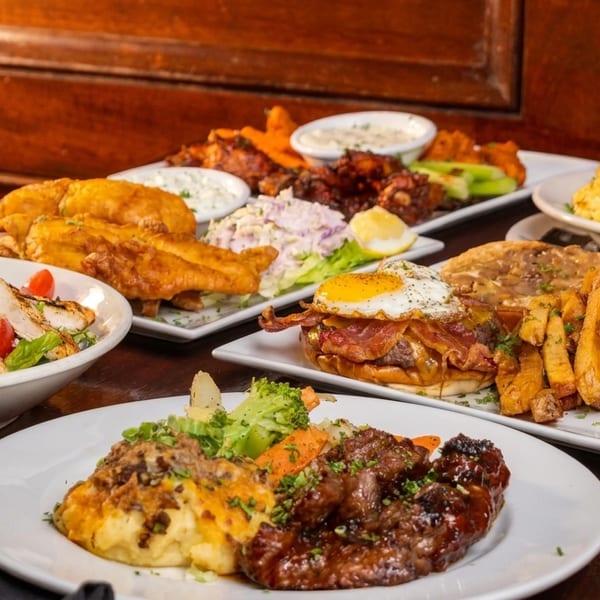A table laden with various dishes, including fish and chips, salad, steak, and a burger.