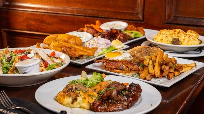 A table laden with various dishes, including fish and chips, salad, steak, and a burger.