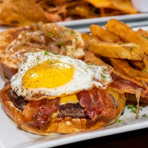 A burger with bacon, cheese, and a fried egg, served with a side of golden french fries.