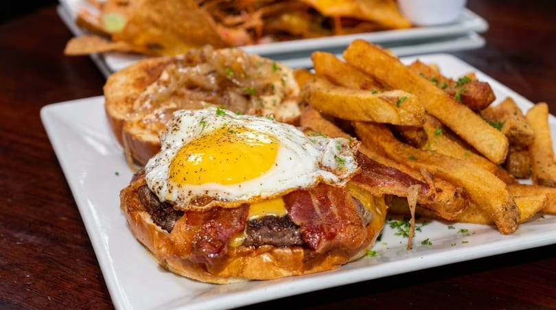 A burger with bacon, cheese, and a fried egg, served with a side of golden french fries.