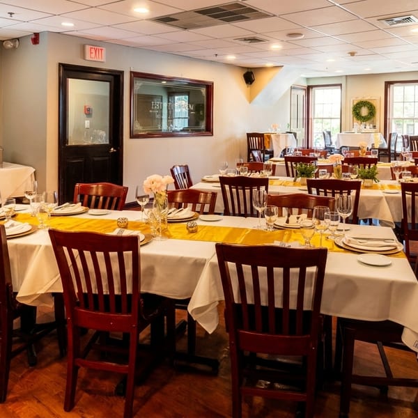 A restaurant dining room with multiple tables set with white tablecloths, yellow runners, and place settings.