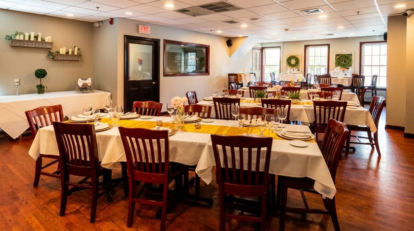 A restaurant dining room with multiple tables set with white tablecloths, yellow runners, and place settings.