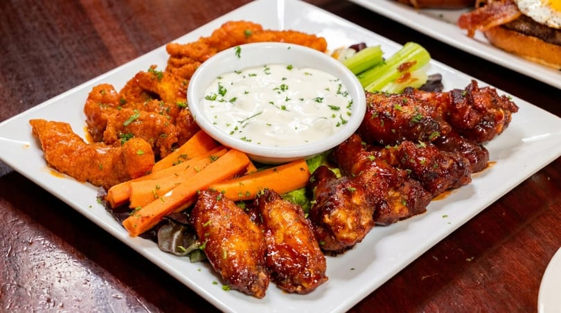 A white platter with buffalo wings, barbecue wings, carrots, celery, and ranch dressing.