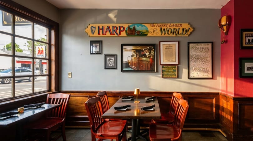 Cozy Irish pub interior with wooden tables, red chairs, Harp Lager sign, and framed pictures.